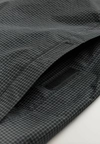 Țesătură neagră cu un model în grilă, având o textură netedă și o peticulă Velcro pe margine, concepută pentru închidere sau atașare.