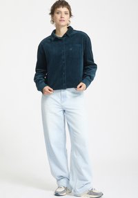 Teal kord när skjorta med spetsig krage, knappar fram och bröstficka, i kombination med ljusblå vida jeans och sneakers.