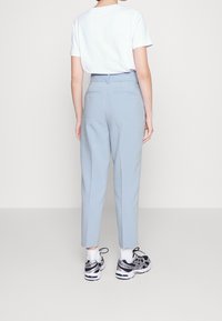 Světle modré kalhoty na míru s hladkou texturou, vybavené dvěma zadními kapsami, v kombinaci s jednoduchým bílým tričkem a černými sportovními botami.