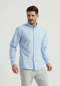 Chemise boutonnée à manches longues bleu clair en tissu doux, avec un col pointu, un placket avant et une coupe ajustée.