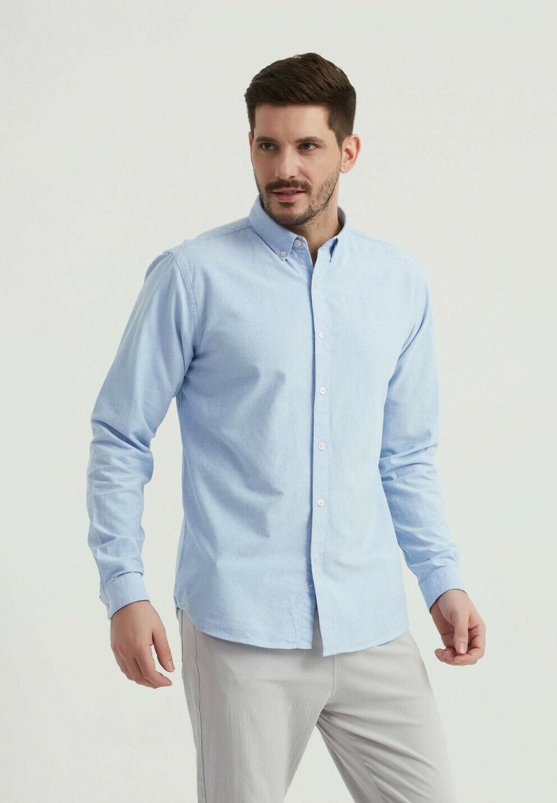 Chemise boutonnée à manches longues bleu clair en tissu doux, avec un col pointu, un placket avant et une coupe ajustée.