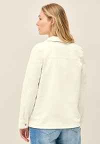 Vaaleanvärinen farkkupaita, jossa on kudottu kuvio, pitkät hihat ja kaulus. Sisältää nappikaitaleet ja rentoa istuvuutta. Taustapuoli näkyy.