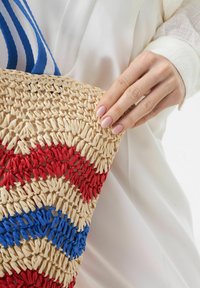 Geweven straw tote bag met rode en blauwe zigzagpatronen, voorzien van gestructureerde natuurlijke vezels en blauwe gestreepte stoffen handvatten.