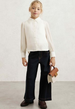 Valge nööbid üles pluus puffed varrukatega, sakilise äärega, koos tumedate laia säärega teksapükste ja väikese kahetoonilise käekotiga.