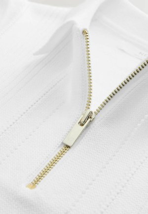 Fehér cipzáras felső arany cipzárral, bordázott mintázatú texturált anyagból, álló gallérral. A cipzár húzója fémes, polírozott felületű.