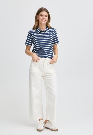 Polo a maniche corte blu navy e bianche a righe abbinato a pantaloni bianchi a vita alta e gamba larga, con sneakers beige.