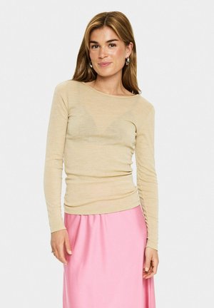 Haut beige à manches longues en tissu léger et transparent avec un col rond. Porté avec une jupe rose fluide. Design minimaliste, texture douce.