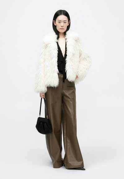 Biela umelá kožušina, čierny hlboký top s výstrihom do V, hnedé široké kožené nohavice a malá čierna kabelka. Hladká textura a objemový tvar.
