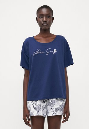 Navy blue cotton t-shirt with a relaxed fit, featuring a white "Vitamin Sea" graphic. Paired with white shorts printed with sea-themed patterns.