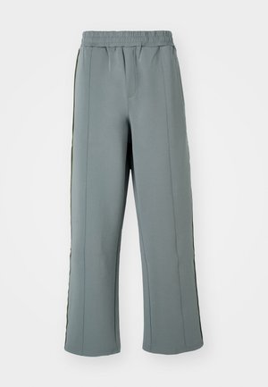 Pantaloni grigi in felpa realizzati in tessuto morbido, dotati di vita elastica e strisce verticali a contrasto lungo i lati. Design morbido.