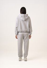 Szürke, oversized kapucnis pulóver húzózsinórral, amely párosítva van a hozzá illő melegítőnadrággal. Mindkettő bordázott szegéllyel és puha tapintással rendelkezik.