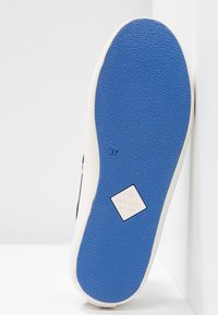 Semelle de basket blanche avec une semelle inférieure en caoutchouc bleu texturé, dotée d'un logo en forme de diamant et d'une impression de taille "37". Design épuré avec des accents minimaux.