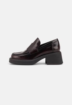 Mocassin en cuir marron foncé avec un talon bloc noir épais et une large bride à l'avant, vu de côté sur fond blanc.