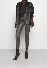 Svart läderskjorta, mörk linne, grå åtsittande byxor och sandaletter med hög klack och guldaccenter. Slät textur och skräddarsydd passform.