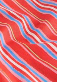 Červená tkanina s vlnitými pruhmi v modrej, ružovej a zelenej farbe. Textúra je hladká s jemným leskom, vytvárajúc dynamický vzor.