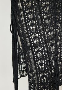 Îmbrăcăminte din dantelă neagră, cu un model floral croșetat sofisticat, textură cu țesătură deschisă și detalii ajustabile cu șnur pe laterale.