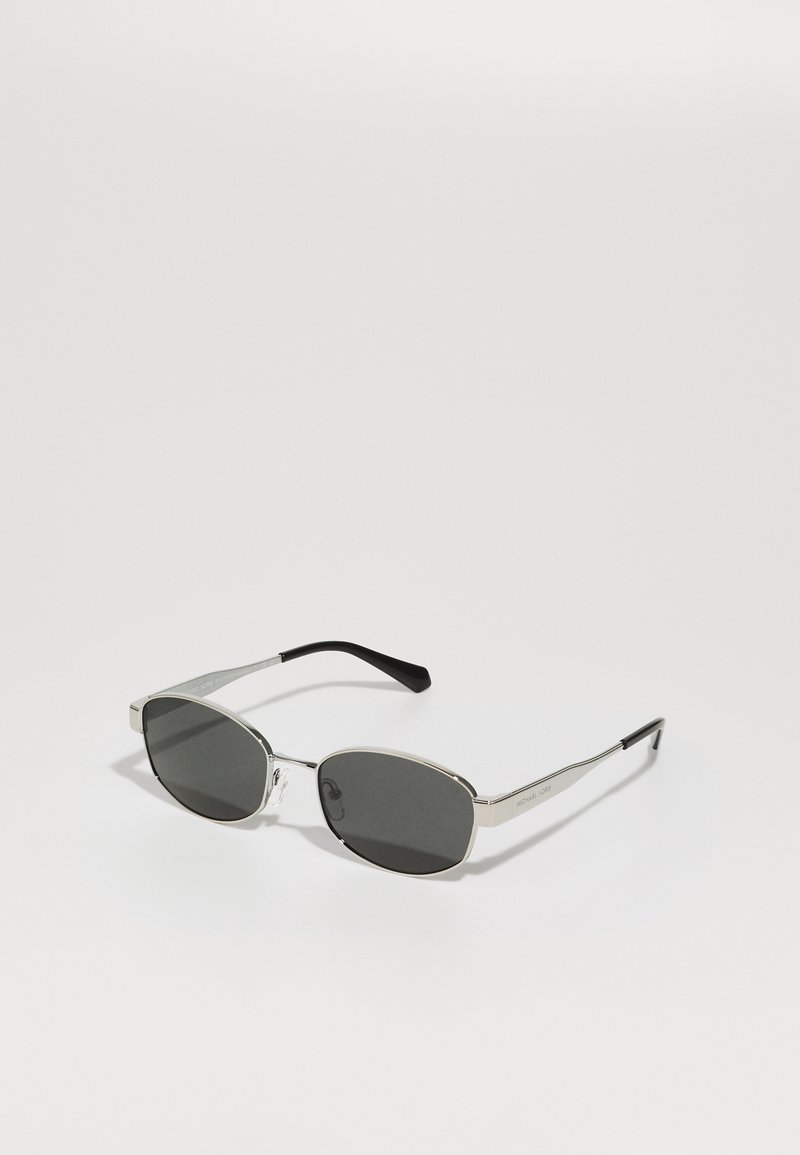 Ochelari de soare cu lentile gri, ramă subțire din metal argintiu, accente transparente și vârfuri negre pe brațe. Au o formă ovală.