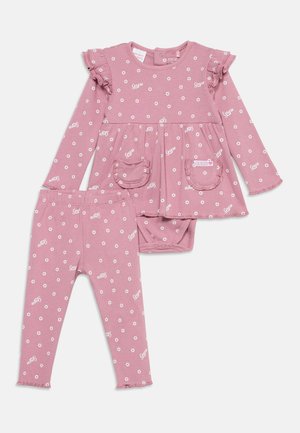 Robe bébé rose à manches longues avec de petites fleurs blanches et texte "Guess", accompagnée de leggings assortis, avec poches à volants et boutons-pression.