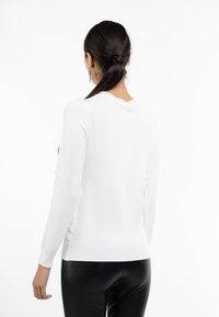 Hvid langærmet sweater med en tekstureret overflade, ribbede manchetter og en bølgemasket halsudskæring, båret over sorte faux læderbukser.