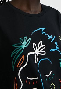 Svart bomullst-shirt med färgglatt blomstermönster och abstrakt ansiktsdesign; inkluderar blåa, gröna, orange och vita accenter. Rund halsringning, avslappnad passform.