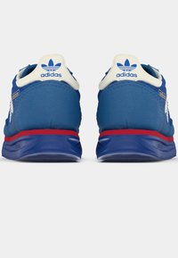 Zili sporta apavi zilā krāsā ar baltām akcentēm, sarkano vidusdaļu un ar paraksta adidas logotipu uz papēža. Iespējots teksturēts auduma virspusējs slānis un mīkstināta zole.