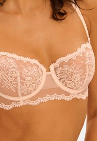 Lyserød blonde-bh med blomsterbroderi, bølgede kanter og et gennemsigtigt mesh-design. Let polstrede skåle med justerbare stropper.