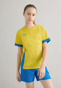 Ungdomsidrottsutrustning med en ljusgul kortärmad tröja med blå accenter och matchande blå shorts. Tillverkad av ett lätt material.