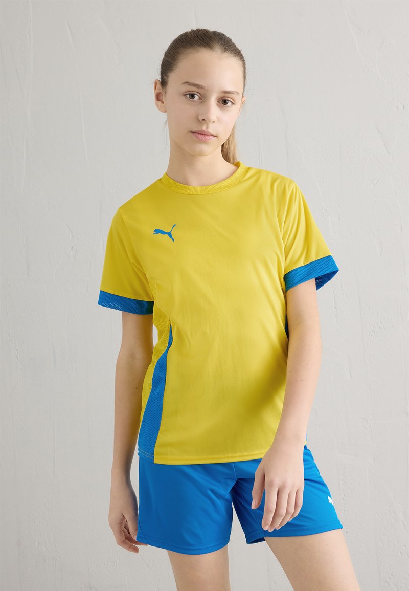 Ungdomsidrottsutrustning med en ljusgul kortärmad tröja med blå accenter och matchande blå shorts. Tillverkad av ett lätt material.