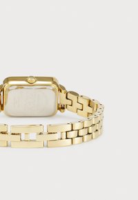 Gold rectangular watch with a metal bracelet. Smooth surface, features a textured back, and a round crown on the side. Simple link design.