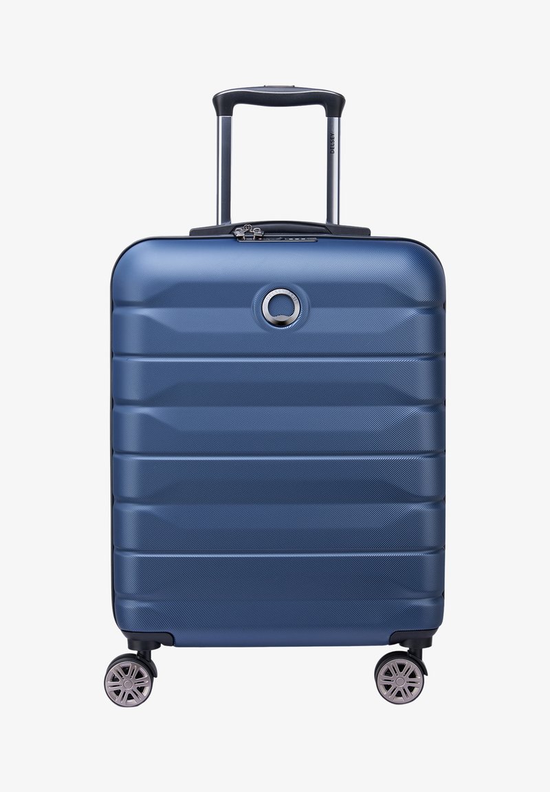 Maleta rígida azul con una superficie texturizada y ondulada, mango retráctil, cuatro ruedas y un emblema circular de marca en la parte frontal.