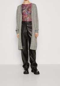 Šedý pletený cardigan s dlouhými rukávy, doplněný o černé kožené kalhoty a robustní černé boty. Vrchní díl má fialový květinový vzor.