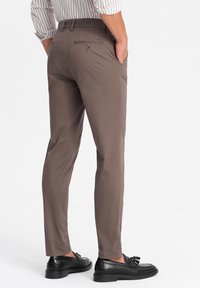 Slim-fit kalhoty z lehké hnědé bavlněné tkaniny. Plochý přední díl, zadní kapsy na knoflíkový uzávěr a lemované manžety. Černé boty doplňují vzhled.