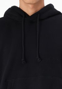 Sweatshirt preto com cordão, apresentando uma textura suave, bolso canguru e um design de ajuste descontraído.