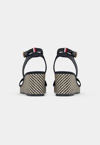 Schwarze Leder-Wedgesandalen mit offener Ferse, ausgestattet mit einem geflochtenen, tanfarbenen und schwarz gestreiften Absatz sowie einem dekorativen rot-weißen Streifen am Riemen.