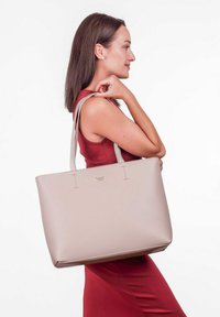 Beige kabelka z umělé kůže s dlouhými, světle šedými popruhy, charakterizovaná minimalistickým designem, zlatým logem a otevřeným vrchem pro snadný přístup.