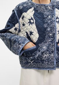 Διπλωμένη ζακέτα σε ναυτικό και κρεμ χρώμα με λουλουδάτα και αστρικά μοτίβα. Διαθέτει φαρδιά μανίκια και πλαϊνές τσέπες. Υφή υφάσματος με διακοσμητική ταινία.