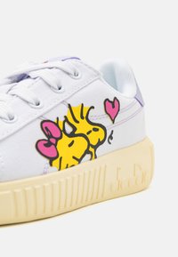Baskets en toile blanches avec des graphiques d'animaux de dessin animé jaunes, des accents lavande et une semelle en crème texturée présentant des rainures verticales.