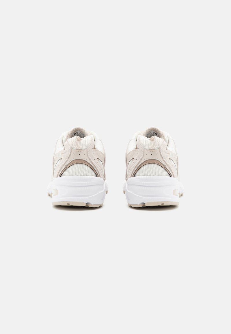 Le scarpe da atletica beige e bianche presentano una tomaia testurizzata, una suola ammortizzata e un design arrotondato con un branding minimalista sul tallone e sulla linguetta.