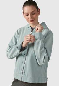 Giacca azzurra chiaro con cappuccio, chiusura con zip, polsini con bottoni e taschino sul petto. Realizzata in tessuto morbido e testurizzato con un fit casual.