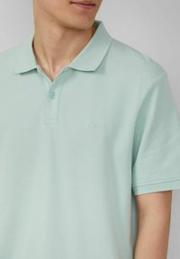 Hellgrünes Polohemd aus strukturiertem Gewebe, mit einem Kragen, zwei Knöpfen und einem dezenten Markenlogo auf der Brust.