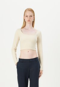Top a maniche lunghe accorciato color crema con texture a coste e scollo quadrato, abbinato a pantaloni navy con chiusura a pulsante.