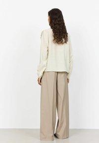 Hellbeige Langarmshirt mit gerafften Manschetten, kombiniert mit lockeren beigen Hosen. Weicher, strukturierter Stoff; minimalistisches Design.