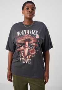 T-shirt surdimensionné gris foncé avec un graphique coloré de champignon et le texte "AMOUR DE LA NATURE" en police audacieuse et fantaisiste. Matière en coton, coupe décontractée.