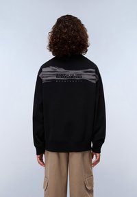 Sudadera negra con acentos texturizados grises en la parte posterior, que presenta un logotipo prominente. Puños y dobladillo acanalados, corte relajado.
