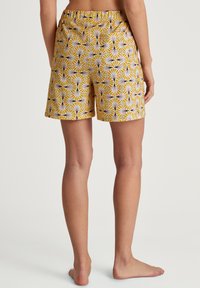 Patroonshorts met een gele achtergrond. Voorzien van een herhalend ontwerp van waaiervormen in paars en wit. Elastische band, knielange snit.