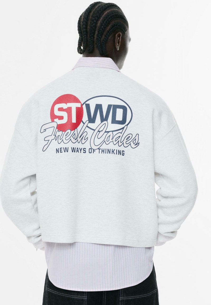 Vaalean harmaa lyhyt hiha-sweatshirt, jossa on brodeerattu logo punaisella ja laivastonsinisellä, takana lukee "Fresh Codes" ja "New Ways of Thinking".