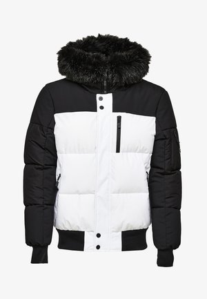 Vaatteet, joissa on musta yläosa ja valkoinen alaosa, tekoturkista vuorattu huppu, vetoketjulliset taskut sekä ribatut hihansuut ja helma.