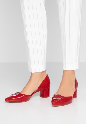 Røde laklæder block-heel sko med spids tå og en hjerteformet metallisk detalje foran. Båret med hvidstribede bukser.