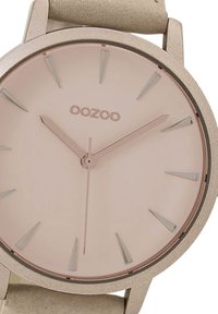 Montre à quartz avec un cadran rose poudré, marqueurs d'heure minimalistes, bracelet en cuir beige clair et boîtier en métal texturé et mat.