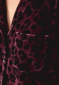 Burgundia sametist pidžaamakampsun musta leopardi mustriga. Omab rinna taskut ja sarnaneb satiinile.